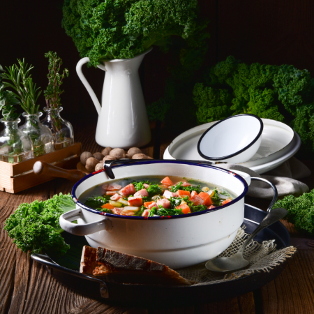 Una olla de sopa de verduras con zanahorias, col rizada y hierbas, rodeada de ingredientes frescos y utensilios de cocina rústicos. La comida como medicina.