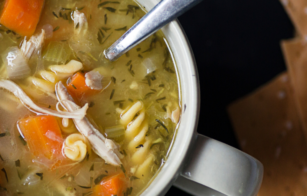 A bowl of chicken noodle soup with carrots, celery, and herbs, accompanied by crackers.
