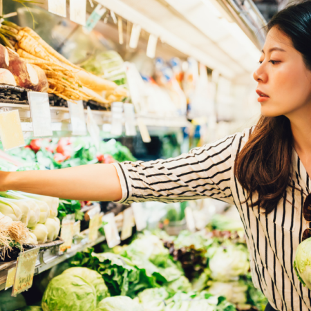 Una mujer haciendo la compra, seleccionando verduras frescas. Considera consejos para ahorrar dinero en medio de la inflación alimentaria.