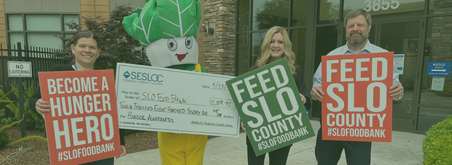 People hold signs for a food bank donation event, featuring a mascot and a large check for $12,871.92.