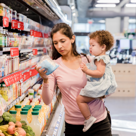 A woman carrying a child is shopping in a grocery store, examining a product with sale tags around.
