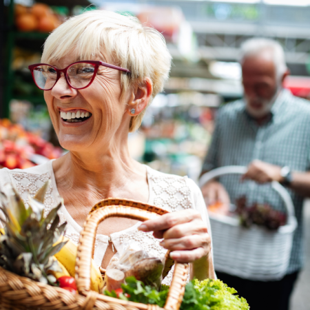 A smiling woman holding a basket of fresh produce at a market, suggesting a place where to use CalFresh EBT.